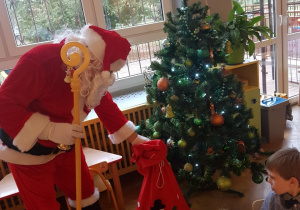 Mikołaj stawia prezenty pod choinką